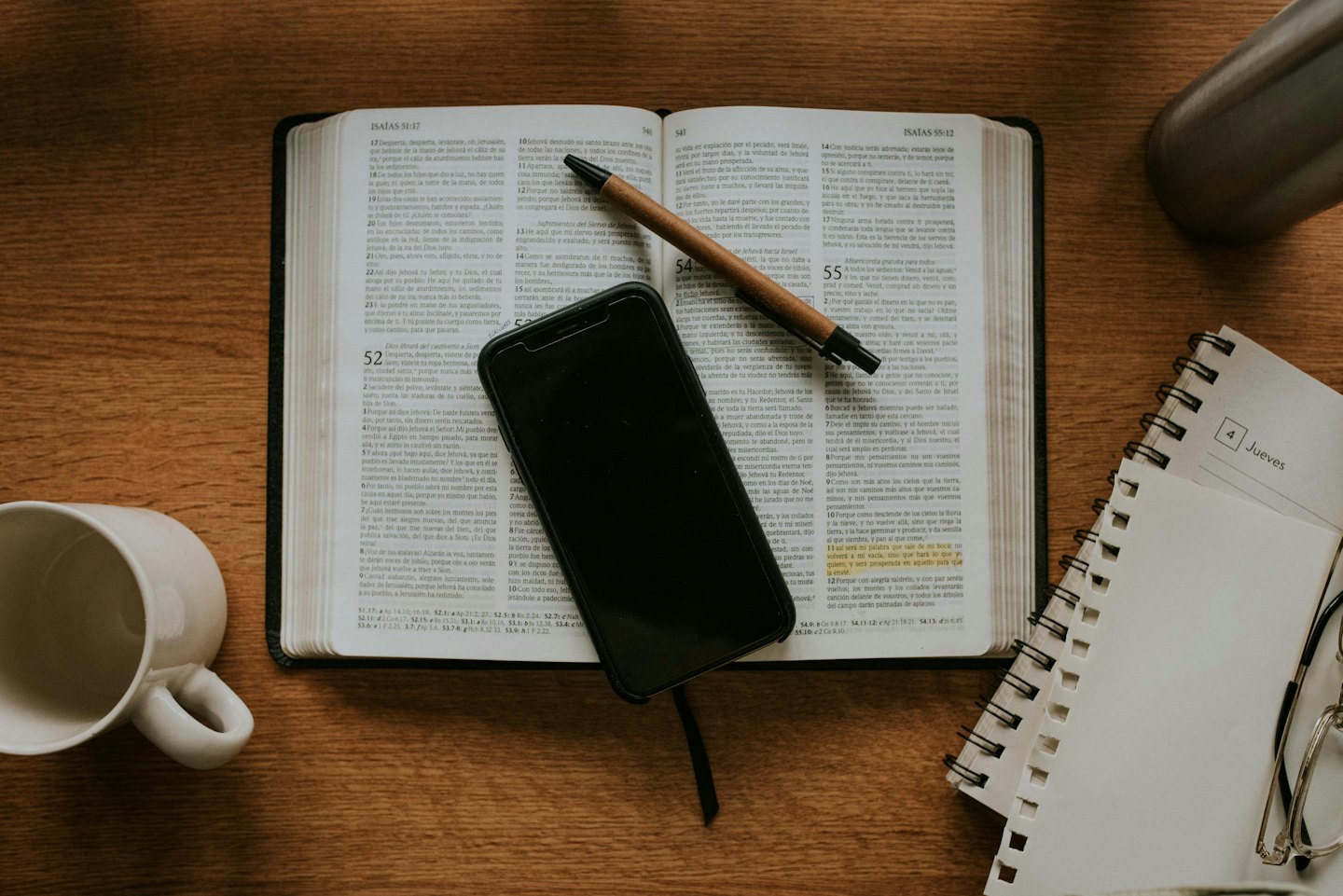 Open Bible with smartphone and pen on a wooden desk.